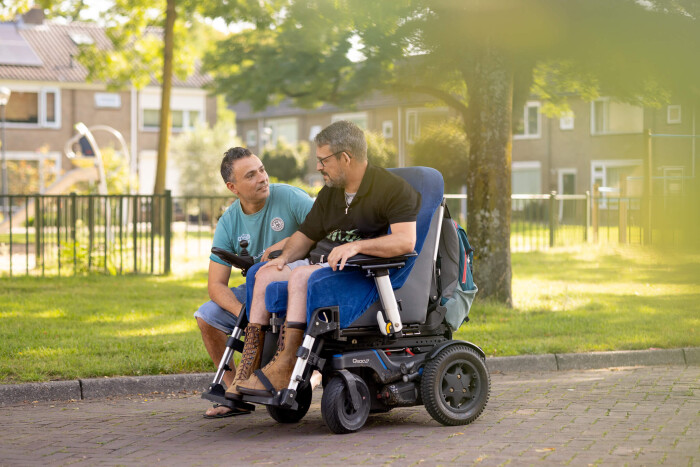 Begeleider Rachid maakt een wandeling in het park met een cliënt in een rolstoel.