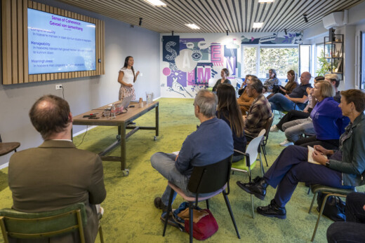 Trainer Tessa legt theorie uit voor een groep deelnemers die voor haar zitten.