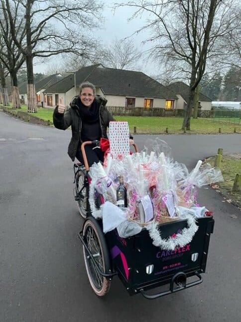 Zorgmanager Anouk zit op een bakfiets vol met wintertour pakketten en steekt lachend haar duim op.