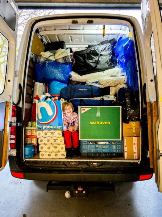 Een bus tot het plafond volgeladen met voeding en levensmiddelen. Een kindje zit tussen alle spullen in.